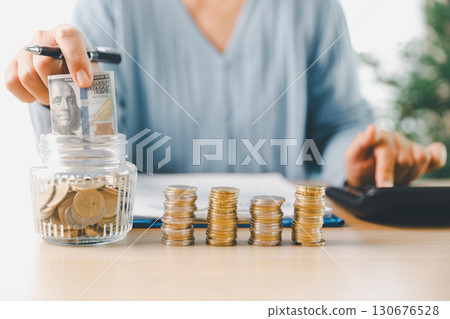 Hand places coin into saving jar, representing how smart finance, investment, banking practices turn money, cash, currency into financial wealth drives business growth and strengthens the economy. 130676528
