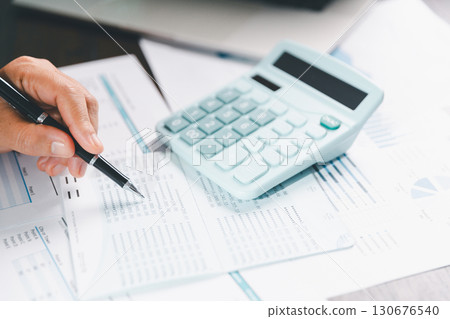 Auditor reviews financial statement and balance sheet on desk using a calculator, representing the concept of accounting, audit, and finance in preparing a detailed financial report for the business. 130676540