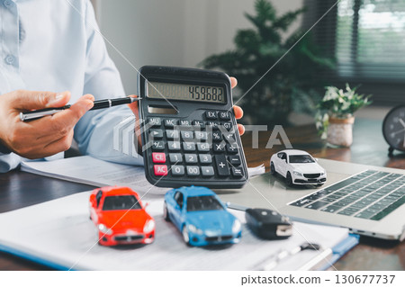 Businesswoman signing car insurance document or lease paper. Writing signature on contract or agreement. Buying or selling new or used vehicle. Car keys on table. Warranty or guarantee. Businesswoman signing car insurance document or lease paper. Writing signature on contract or agreement. Buying or selling new or used vehicle. Car keys on table. Warranty or guarantee. 130677737