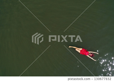 Woman in a red dress floating in water aerial view 130677832