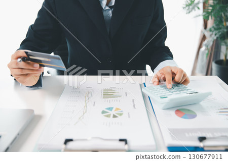 Accountant working on desk using calculator for calculate finance report in office. business finance, calculate tax by organizing financial documents, tracking income investment, accounting by hand. Accountant working on desk using calculator for calculate finance report in office. business finance, calculate tax by organizing financial documents, tracking income investment, accounting by hand. 130677911