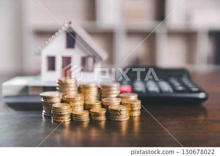 Model house, stacks of coins, calculator, financial documents on a wooden desk represent real estate investment and mortgage planning, highlighting financial growth and strategic planning strategies. 130678022