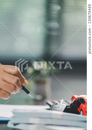 Business office, woman employee finalizes deal with client, handing over car key after signing contract and reviewing insurance and loan documents for sale or rent of vehicle at table. 130678489