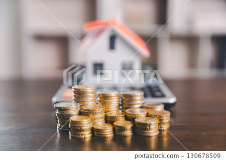 Model house, stacks of coins, calculator, financial documents on a wooden desk represent real estate investment and mortgage planning, highlighting financial growth and strategic planning strategies. 130678509