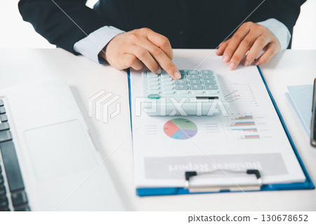 Accountant working on desk using calculator for calculate finance report in office. business finance, calculate tax by organizing financial documents, tracking income investment, accounting by hand. 130678652