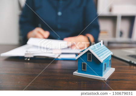 House model placed on table alongside coins, paperwork symbolizes real estate investment, property valuation, representing financial planning, mortgage options, market analysis in property business. 130679031