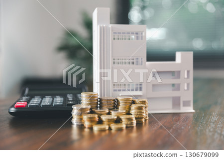 Model house, stacks of coins, calculator, financial documents on a wooden desk represent real estate investment and mortgage planning, highlighting financial growth and strategic planning strategies. Model house, stacks of coins, calculator, financial documents on a wooden desk represent real estate investment and mortgage planning, highlighting financial growth and strategic planning strategies. 130679099