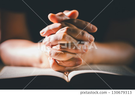 Hands clasped in prayer over the holy Bible, the faithful Christian worships God in church, holding onto hope and belief, guided by religion and a deep commitment to their religious faith. 130679313