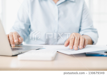 Concept of business finance and accounting. Businessman works with laptop, financial documents on office desk, analyzing tax report, budget management and corporate financial planning with accuracy. Concept of business finance and accounting. Businessman works with laptop, financial documents on office desk, analyzing tax report, budget management and corporate financial planning with accuracy. 130679349