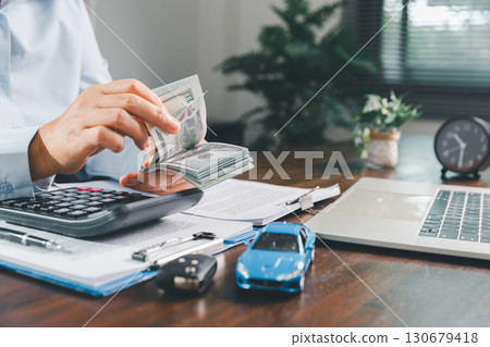 Businesswoman signing car insurance document or lease paper. Writing signature on contract or agreement. Buying or selling new or used vehicle. Car keys on table. Warranty or guarantee. 130679418