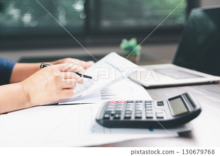 Office businesswoman hand to operate calculator analyzing financial data, counting costs on desk. accounting, financial analysis for business budget planning, calculation support, finance management. Office businesswoman hand to operate calculator analyzing financial data, counting costs on desk. accounting, financial analysis for business budget planning, calculation support, finance management. 130679768