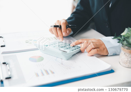 Accountant working on desk using calculator for calculate finance report in office. business finance, calculate tax by organizing financial documents, tracking income investment, accounting by hand. Accountant working on desk using calculator for calculate finance report in office. business finance, calculate tax by organizing financial documents, tracking income investment, accounting by hand. 130679770