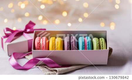 Gift box with colorful macarons and pink ribbon on soft fabric background, festive sweet treat with warm lights. Gift box with colorful macarons and pink ribbon on soft fabric background, festive sweet treat with warm lights. 130679842