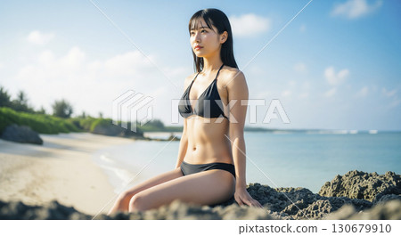 A profile shot of a woman in a bikini sitting on a rock and gazing into the distance 130679910