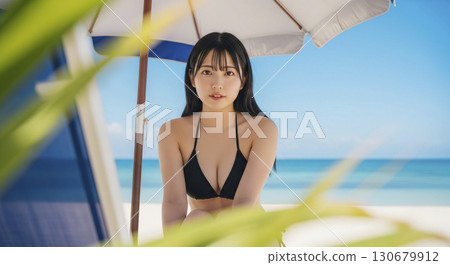 Woman in bikini relaxing in a beach chair under a beach umbrella 130679912
