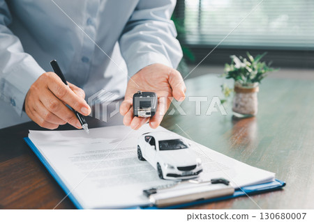 Customer signing insurance document lease agreement table, writing signature contract buying selling new or used vehicle, with car keys, warranty papers, guarantee included in transaction. Customer signing insurance document lease agreement table, writing signature contract buying selling new or used vehicle, with car keys, warranty papers, guarantee included in transaction. 130680007