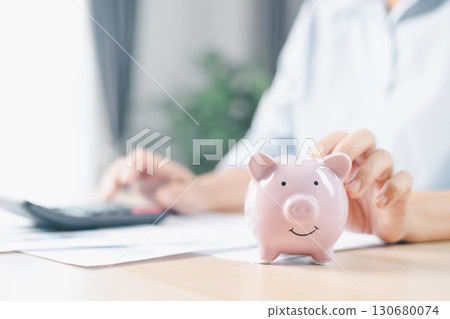Concept of saving money and financial security. Pink piggy bank surrounded by coins on office desk with businesswoman in background, symbolizing investment, wealth growth and budget management. Concept of saving money and financial security. Pink piggy bank surrounded by coins on office desk with businesswoman in background, symbolizing investment, wealth growth and budget management. 130680074