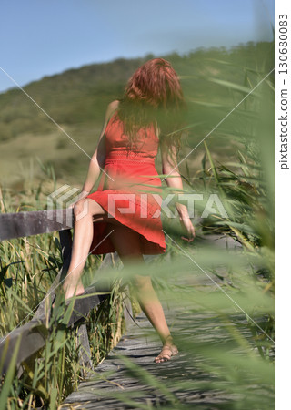 Woman in red dress standing barefoot on wooden footbridge in nature 130680083