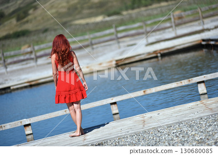 Back view of woman with red hair in red dress by pool 130680085
