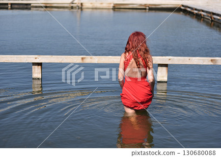 Back view of woman with red hair in red dress by pool 130680088