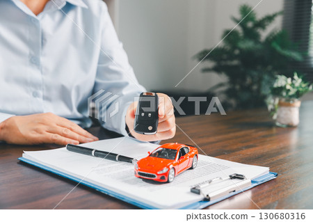 Businesswoman signing car insurance document or lease paper. Writing signature on contract or agreement. Buying or selling new or used vehicle. Car keys on table. Warranty or guarantee. 130680316