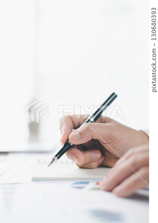 Concept of business planning and financial analysis. A businesswoman writes notes on documents with charts and reports, using laptop and calculator for budget management at modern office desk. 130680393
