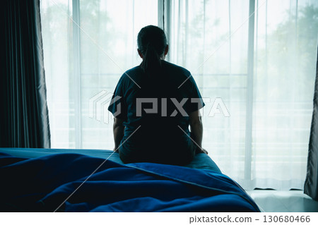 A woman sitting alone on bed facing window in dark room, symbolizing depression, loneliness, anxiety, sadness, mental health struggle, insomnia and emotional stress in life challenges. A woman sitting alone on bed facing window in dark room, symbolizing depression, loneliness, anxiety, sadness, mental health struggle, insomnia and emotional stress in life challenges. 130680466