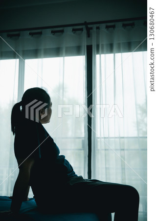 A woman sitting alone on bed facing window in dark room, symbolizing depression, loneliness, anxiety, sadness, mental health struggle, insomnia and emotional stress in life challenges. A woman sitting alone on bed facing window in dark room, symbolizing depression, loneliness, anxiety, sadness, mental health struggle, insomnia and emotional stress in life challenges. 130680467