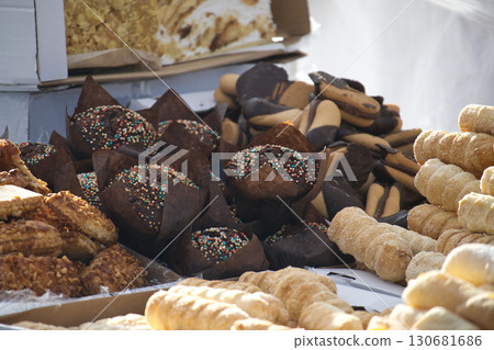 An enticing assortment of muffins, biscuits, and cream rolls are piled high at a bakery stand. An enticing assortment of muffins, biscuits, and cream rolls are piled high at a bakery stand. 130681686