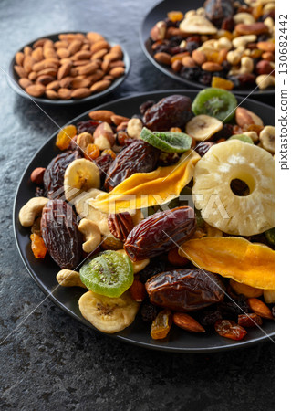 Dried tropical fruits, nuts, and raisins in black plate. 130682442