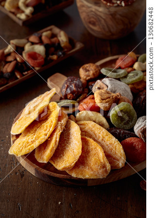 Dried mango slices, tropical fruits, nuts, and raisins on a wooden table. 130682448