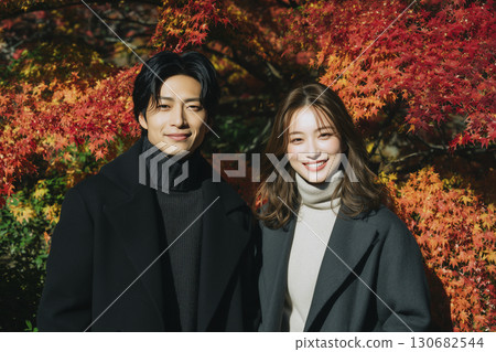 A smiling couple standing with autumn leaves in the background 130682544