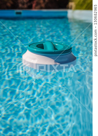 Floating chlorine dispenser drifting in clear blue pool water, used for regular maintenance and water disinfection Floating chlorine dispenser drifting in clear blue pool water, used for regular maintenance and water disinfection 130682965