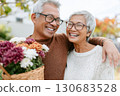 Happy senior couple smiling and embracing outdoors while holding a basket of colorful fresh flowers on a sunny day in the garden Happy senior couple smiling and embracing outdoors while holding a basket of colorful fresh flowers on a sunny day in the garden 130683528