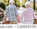 An elderly couple walks hand-in-hand down a peaceful park path on a sunny day, each carrying a wicker basket. A serene and intimate moment of companionship An elderly couple walks hand-in-hand down a peaceful park path on a sunny day, each carrying a wicker basket. A serene and intimate moment of companionship 130683530