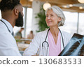 elderly female doctor holding x-ray image and smiling while talking to colleague in modern medical office elderly female doctor holding x-ray image and smiling while talking to colleague in modern medical office 130683533
