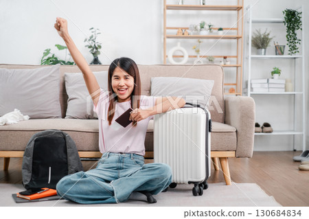 Joyful young woman with passport and suitcase, ready for travel adventure, sitting in a stylish living room. Joyful young woman with passport and suitcase, ready for travel adventure, sitting in a stylish living room. 130684834