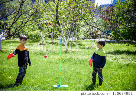 Two friends are playing tetherball swing ball game in summer camping. Two boy brother happy leisure healthy active time outdoors concept Two friends are playing tetherball swing ball game in summer camping. Two boy brother happy leisure healthy active time outdoors concept 130684991