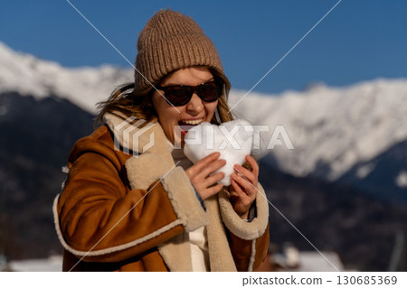 Woman Snow Heart Winter: playfully eating snow heart shaped in sunny mountains. 130685369