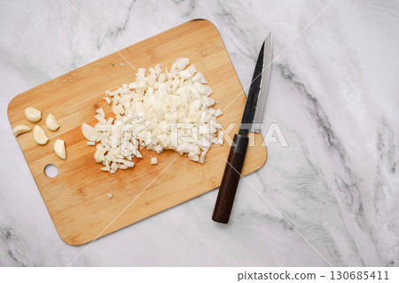Chopping onions and garlic on a wooden cutting board in a modern kitchen Chopping onions and garlic on a wooden cutting board in a modern kitchen 130685411