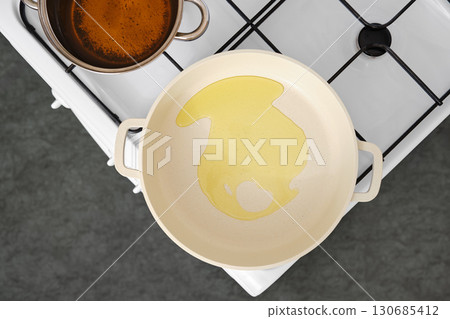 Cooking oil is poured into a frying pan on a stovetop for meal preparation 130685412