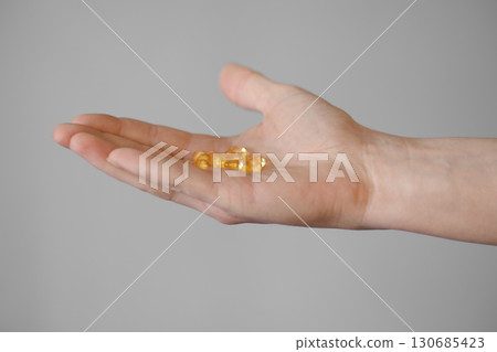 Hand holding several yellow capsules on a neutral background in indoor lighting 130685423
