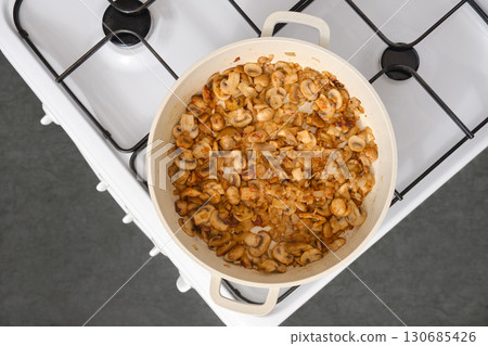 Top view of mushrooms fried in oil in a frying pan on the stove in the kitchen Top view of mushrooms fried in oil in a frying pan on the stove in the kitchen 130685426