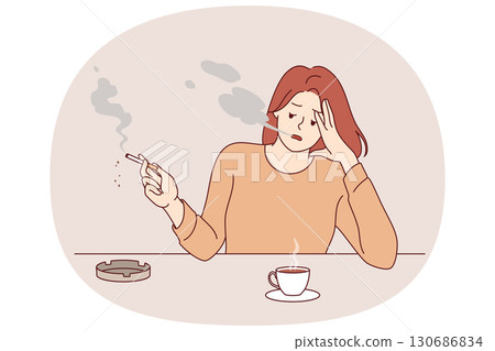 Woman smokes cigarette and drinks hot coffee, sitting at table taking break after difficult work 130686834