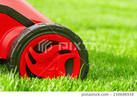 A close-up of a black and red lawn mower mowing on a green lawn. 130686938