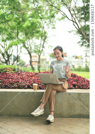 Smiling woman working remotely on laptop in a park, representing the digital nomad lifestyle Smiling woman working remotely on laptop in a park, representing the digital nomad lifestyle 130688117
