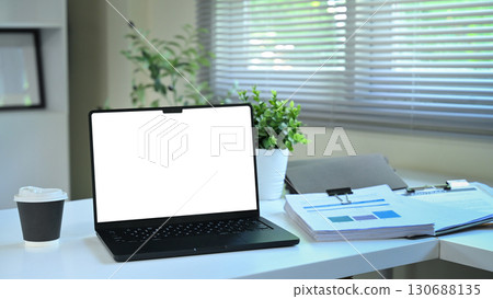 Modern office desk with laptop showing blank screen, coffee cup, documents, and green plant Modern office desk with laptop showing blank screen, coffee cup, documents, and green plant 130688135