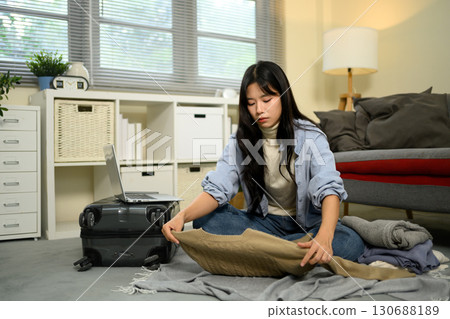 Young woman folding clothes while packing suitcase for an upcoming trip at home 130688189