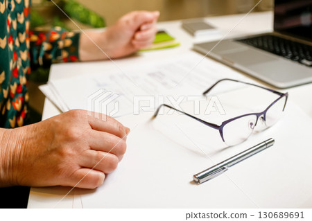 a woman in her workspace, with a focus on her hands and eyeglasses. woman working at laptop hands. professional workspace eyeglasses. home office productivity shot 130689691