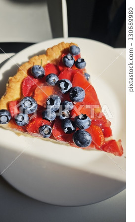 Slice of berry fruit tart with blueberries and strawberries on a white plate in natural light Slice of berry fruit tart with blueberries and strawberries on a white plate in natural light 130689980
